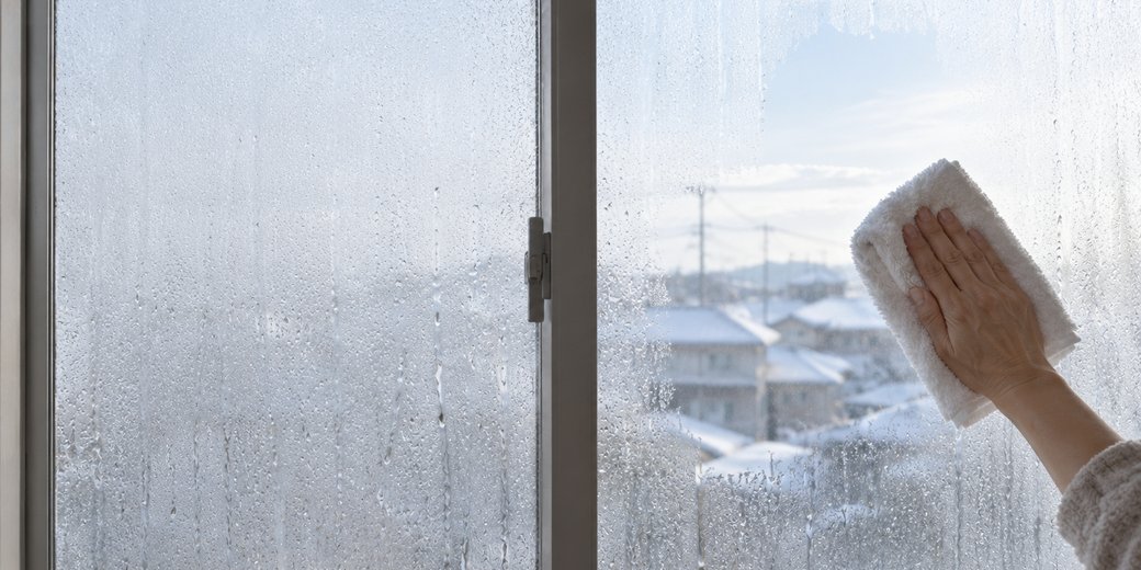 結露で曇った冬の窓を、タオルで拭いている手